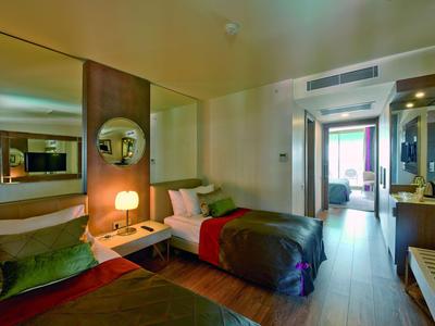 Chambre d'hôtel moderne avec deux lits simples, éclairage chaleureux et accès au balcon.