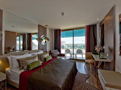 Chambre d'hôtel moderne avec lit double, coin salon et vue sur balcon et mer.