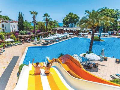 Vista di una piscina dell'hotel con scivoli, palme e ombrelloni in una giornata serena.