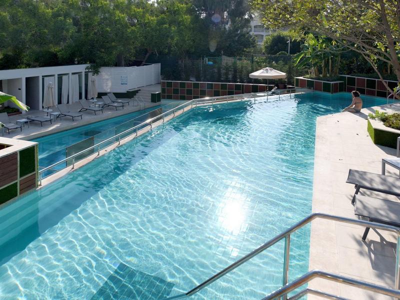 Piscina all'aperto con acqua limpida, circondata da lettini e vegetazione.