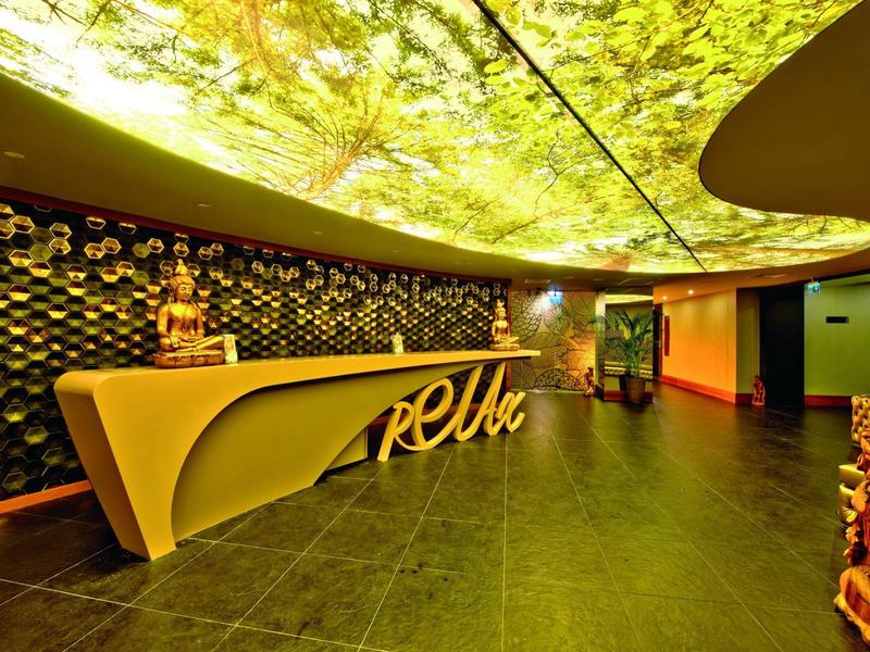 Reception d'hotel luminosa con banco curvo e soffitto illuminato con motivo naturale.