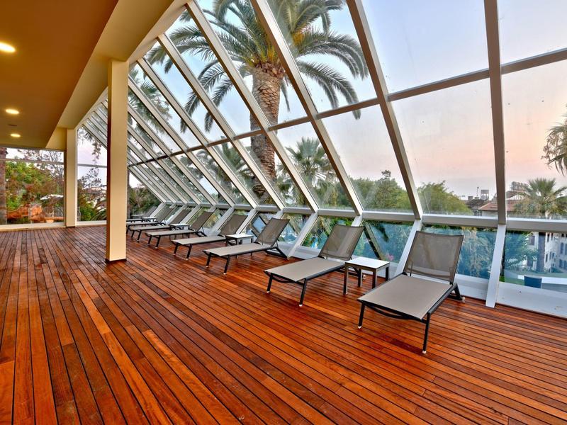 Terrazza coperta con lettini e vista su palme e acqua al tramonto.