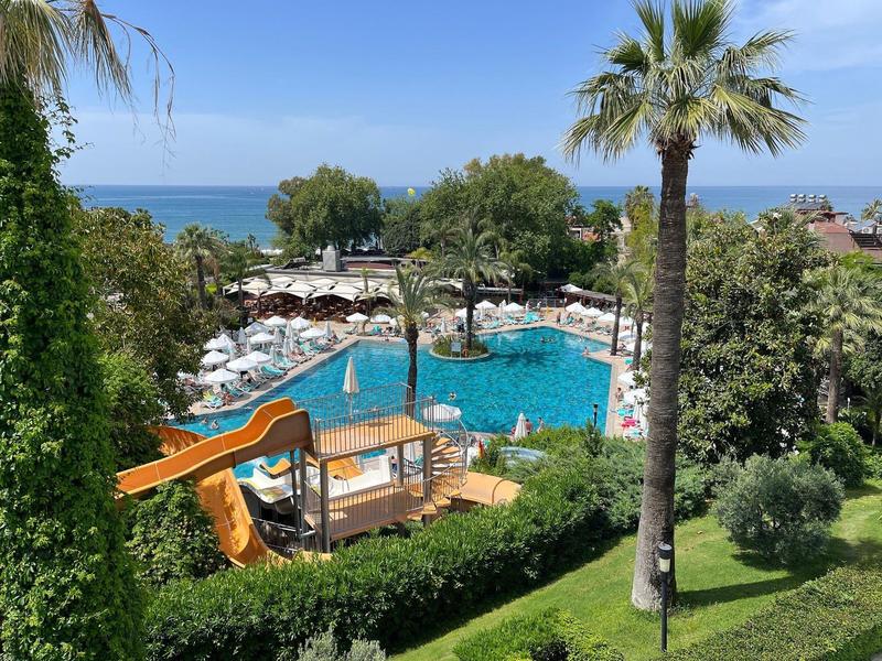 Piscina dell'hotel con scivoli e ombrelloni, circondata da palme e aree verdi con vista mare.
