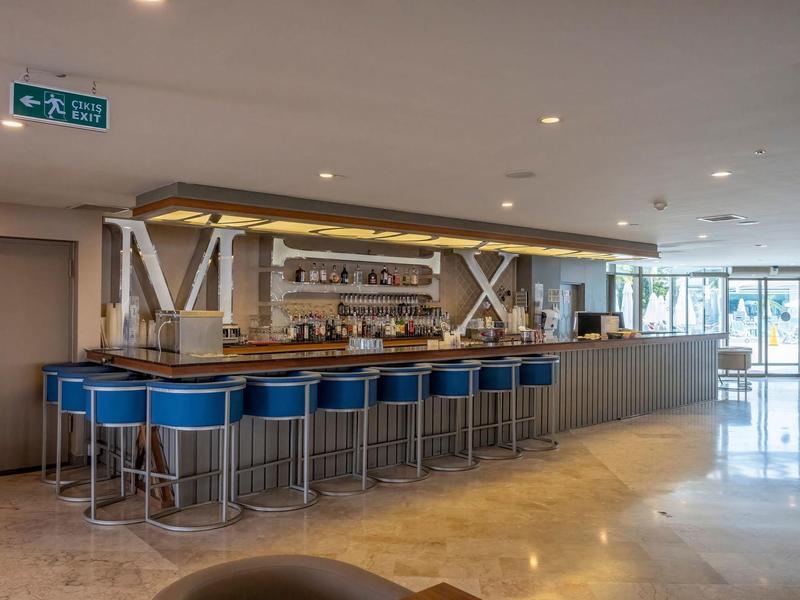 Area bar moderna dell'hotel con sgabelli blu e pavimento chiaro in marmo sotto illuminazione a LED.