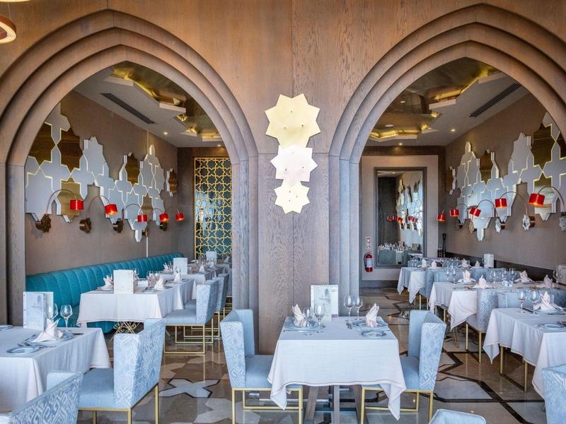 Ristorante elegante con tovaglie bianche, archi curvi e dettagli decorativi alle pareti.