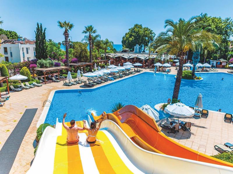 Vista di una piscina dell'hotel con scivoli, palme e ombrelloni in una giornata serena.