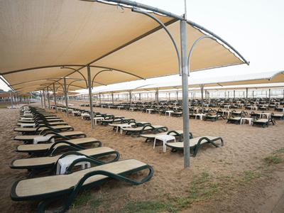 Řada lehátek pod velkými slunečními stínícími plachtami na pláži.