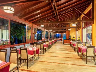 Ampia area ristorante luminosa con soffitto a travi in legno e tavoli con tovaglie rosse.