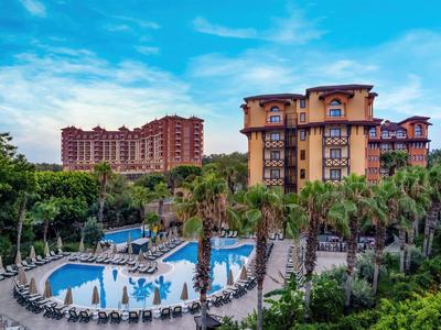 Complesso alberghiero con piscina, palme e lettini sotto un cielo azzurro