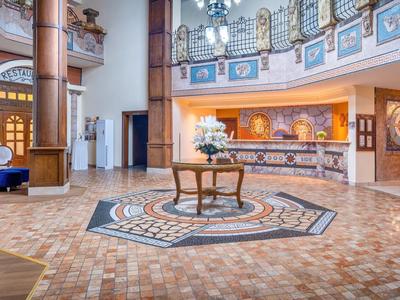 Prostorná hotelová hala s recepcí, posezením a dekorativní podlahovou mozaikou.