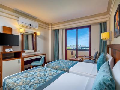 Habitación de hotel con dos camas individuales, escritorio, televisor y balcón con vistas al mar.