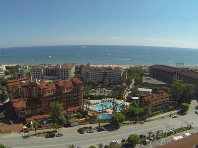 Vista di un hotel con piscina, circondato da edifici e dal mare sullo sfondo.