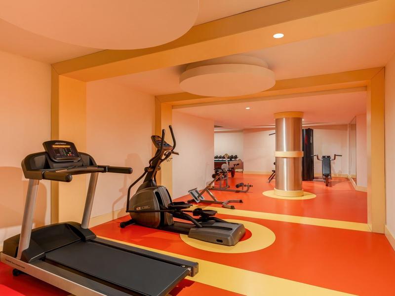 Piccola palestra con tapis roulant, ellittica e grande specchio a parete.