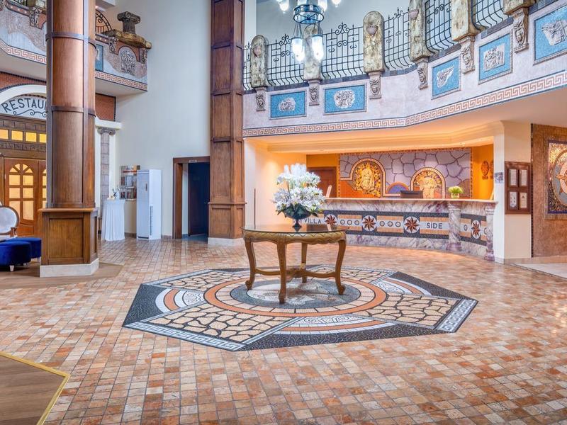 Spaziosa hall d'hotel con pavimento a mosaico, reception e arredamento in legno elegante.