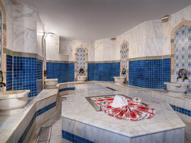 Bagno turco luminoso con piastrelle blu e bianche e bacino centrale in marmo decorato.