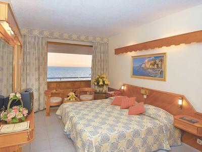 Gemütliches Schlafzimmer mit großem Doppelbett, hellen Vorhängen und Balkon mit Meerblick.