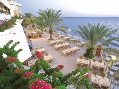 Terrasse avec tables, chaises, palmiers et vue sur la mer dans un hôtel