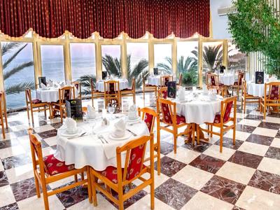 Restaurant élégant avec nappes, mobilier en bois et grandes fenêtres donnant sur des palmiers.