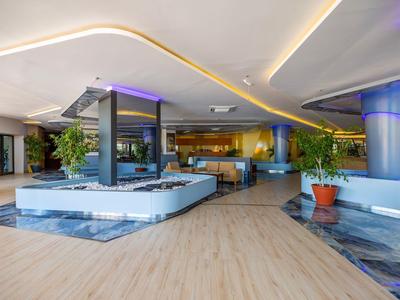 Área lounge moderna de hotel con asientos, plantas e iluminación indirecta.