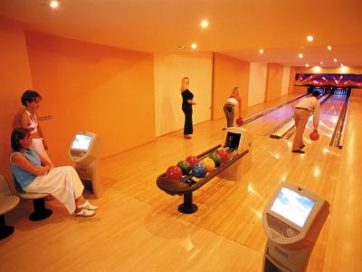Innenraum einer Bowlingbahn mit fünf Menschen, heller Holzboden und orangefarbener Wandbeleuchtung.