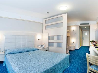 Helles Hotelzimmer mit großem Bett, blauem Teppich und moderner Trennwand zum Flur.