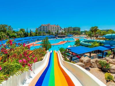 Bunte Wasserrutsche in großem Poolbereich mit Blumen, Bäumen und Hotelgebäuden im Hintergrund.