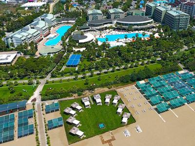 Strandresort mit großen Pools, Sonnenschirmen, grünen Wiesen und türkisfarbenem Meer im Hintergrund.
