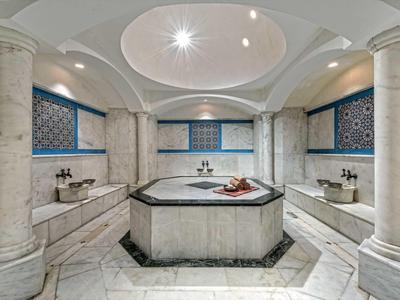 Eleganter Hamam mit Marmor, blau-weißen Fliesen und runden Säulen in symmetrischem Design.
