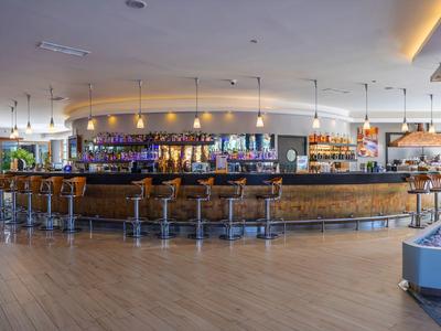 Área de bar moderna en hotel con taburetes de cuero y luz indirecta en el techo.