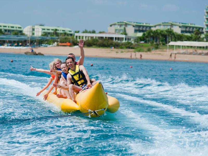 Several people ride a yellow banana boat on the sea near a beach resort.