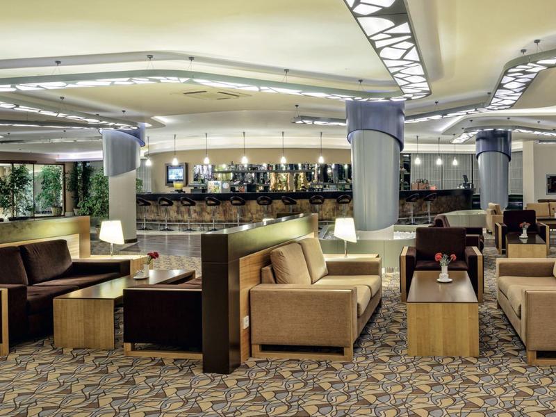 Modern hotel lounge area with comfortable sofas and tables on carpeted floor under bright ceiling lighting.