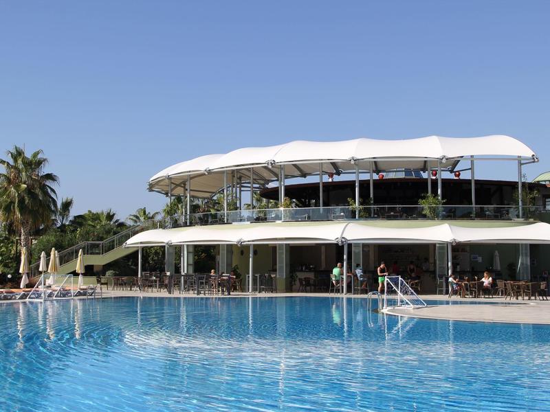 Modern hotel complex with two floors and large outdoor pool under clear sky.