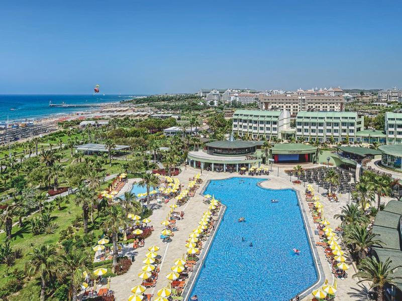 View of a resort with a large pool, palm trees, and beach along the coastline under clear sky.
