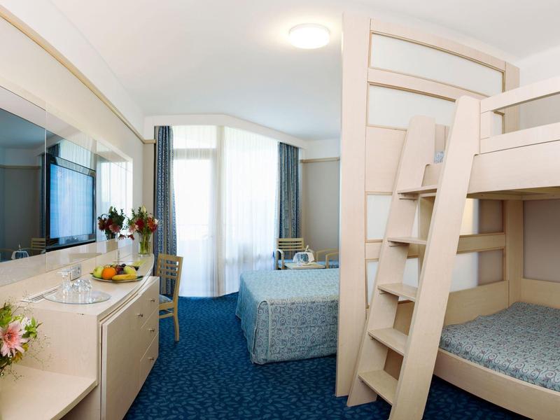 Hotel room with bunk bed, desk, TV, and window with curtains