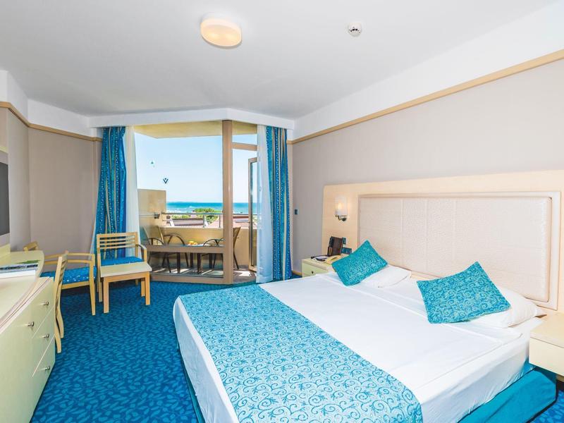 Bright hotel room with double bed, balcony, and sea view.