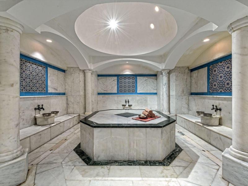 Luxurious spa room with central whirlpool, marble decor, and blue mosaic tiles.
