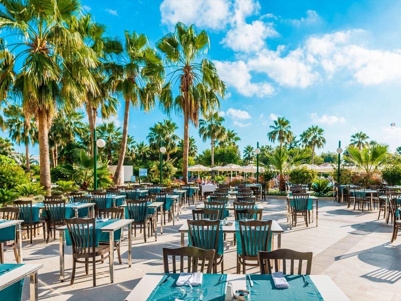 Outdoor restaurant with set tables and palm trees under sunny weather