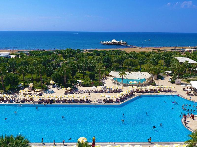 Large pool in front of a hotel overlooking the sea and a marina in the background.