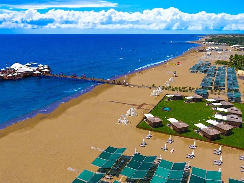 Wide sandy beach with sun loungers and umbrellas along a coastline under clear sky.