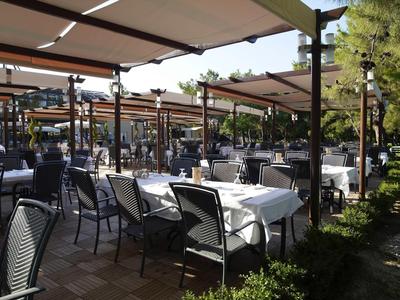 Buitenrestaurant met gedekte tafels en stoelen onder zonneschermen in een hotelsfeer.