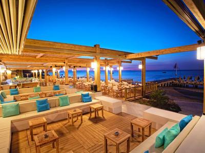 Open strandbar met houten plafonds, banken en uitzicht op zee bij zonsondergang.