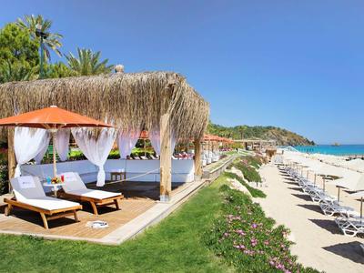 Strandhotel met ligbedden onder rieten cabana's en parasols op het zandstrand.