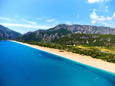 Breed zandstrand langs turquoise zee met bergen op de achtergrond onder een zonnige hemel.