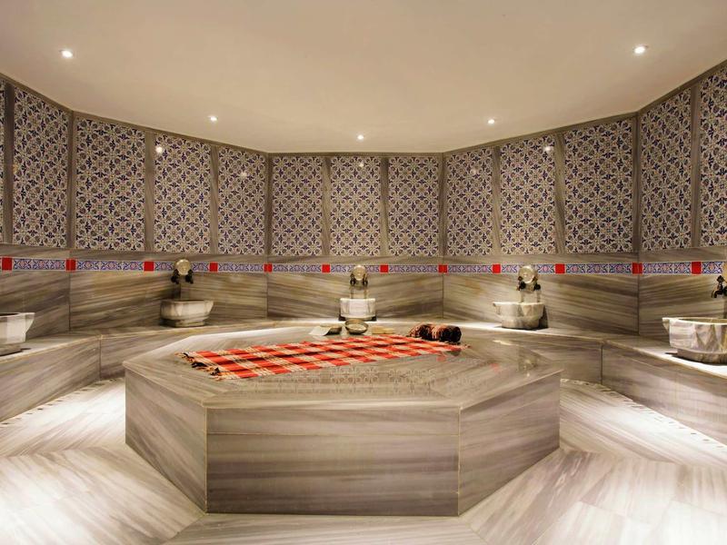 Moderne wellnessruimte met verlicht marmeren fontein en bankzitplaatsen in hammamstijl.