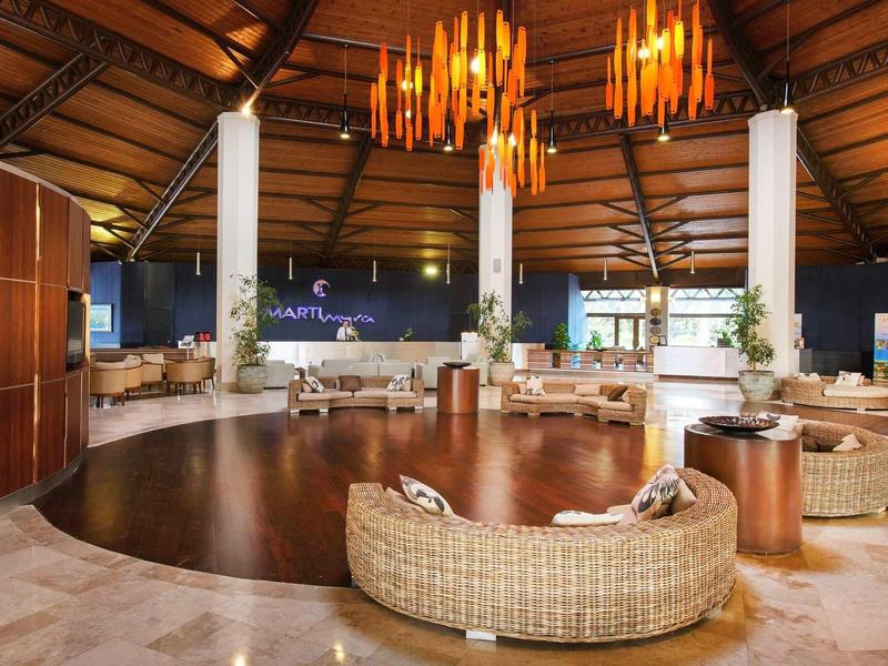 Ruime hotel lobby met moderne rotan stoelen, houten plafond en warme hanglampen.