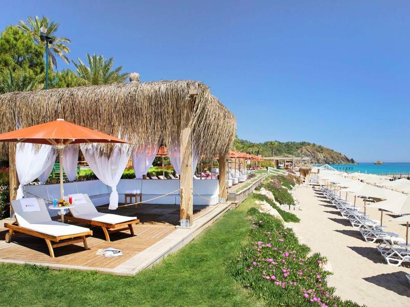 Strandhotel met ligbedden onder rieten cabana's en parasols op het zandstrand.