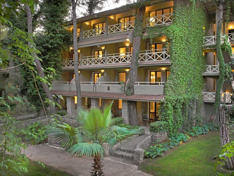 Meerdere verdiepingen tellend hotelgebouw met balkons, omgeven door weelderig groen bij schemering.