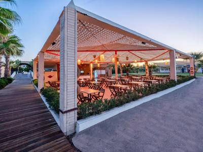 Padiglione aperto con tavoli e sedie in legno accanto a un pavimento in legno e un percorso al tramonto.