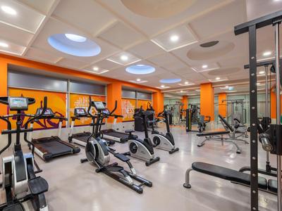 Palestra moderna con tapis roulant, cyclette e attrezzi per pesi, pareti arancioni.