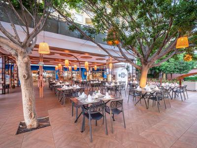 Ristorante all'aperto con tavoli apparecchiati sotto gli alberi sulla terrazza dell'hotel.